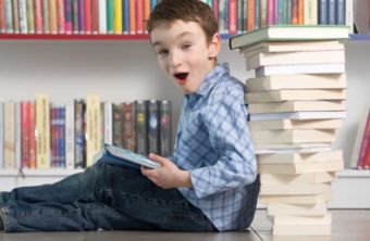 Child excitedly reading a book while leaning against a stack of books
